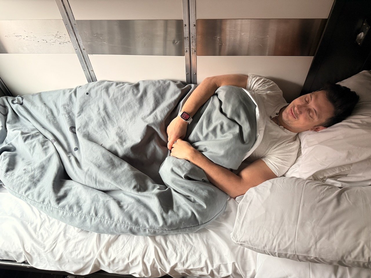 Man sleeping peacefully under a gray blanket on a bed.