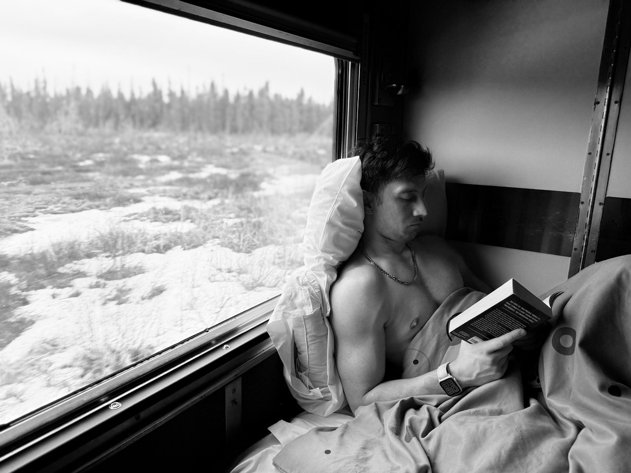 Man reading a book on a train journey, black and white photo.