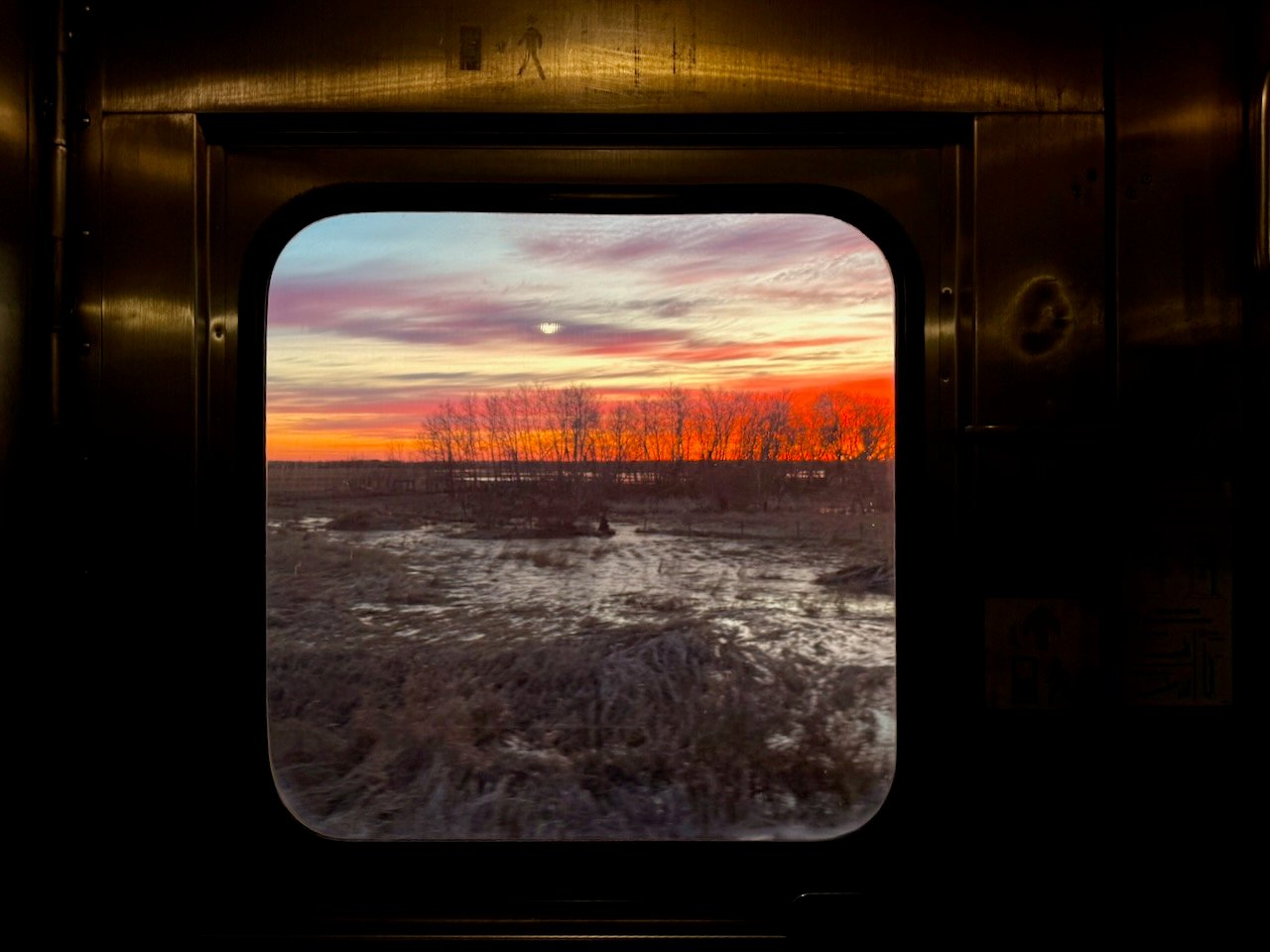 Train window view of vibrant sunset over a rural landscape.