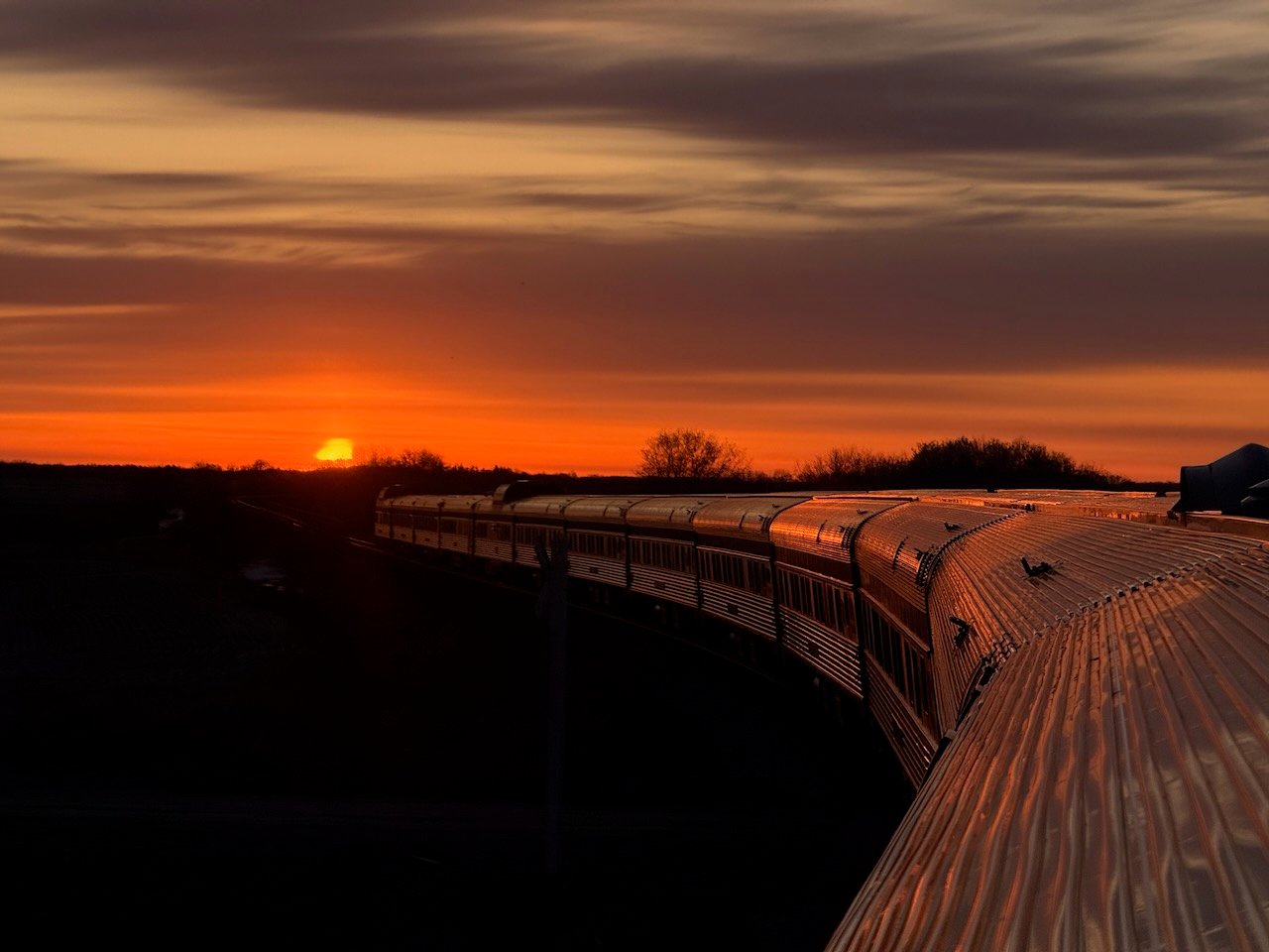 Train at sunset with a glowing sky reflecting on its metallic surface.