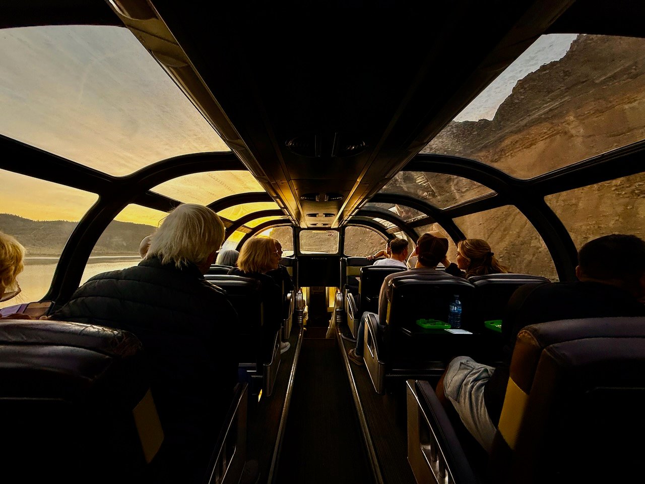 Scenic train ride with passengers and panoramic views through glass roof.