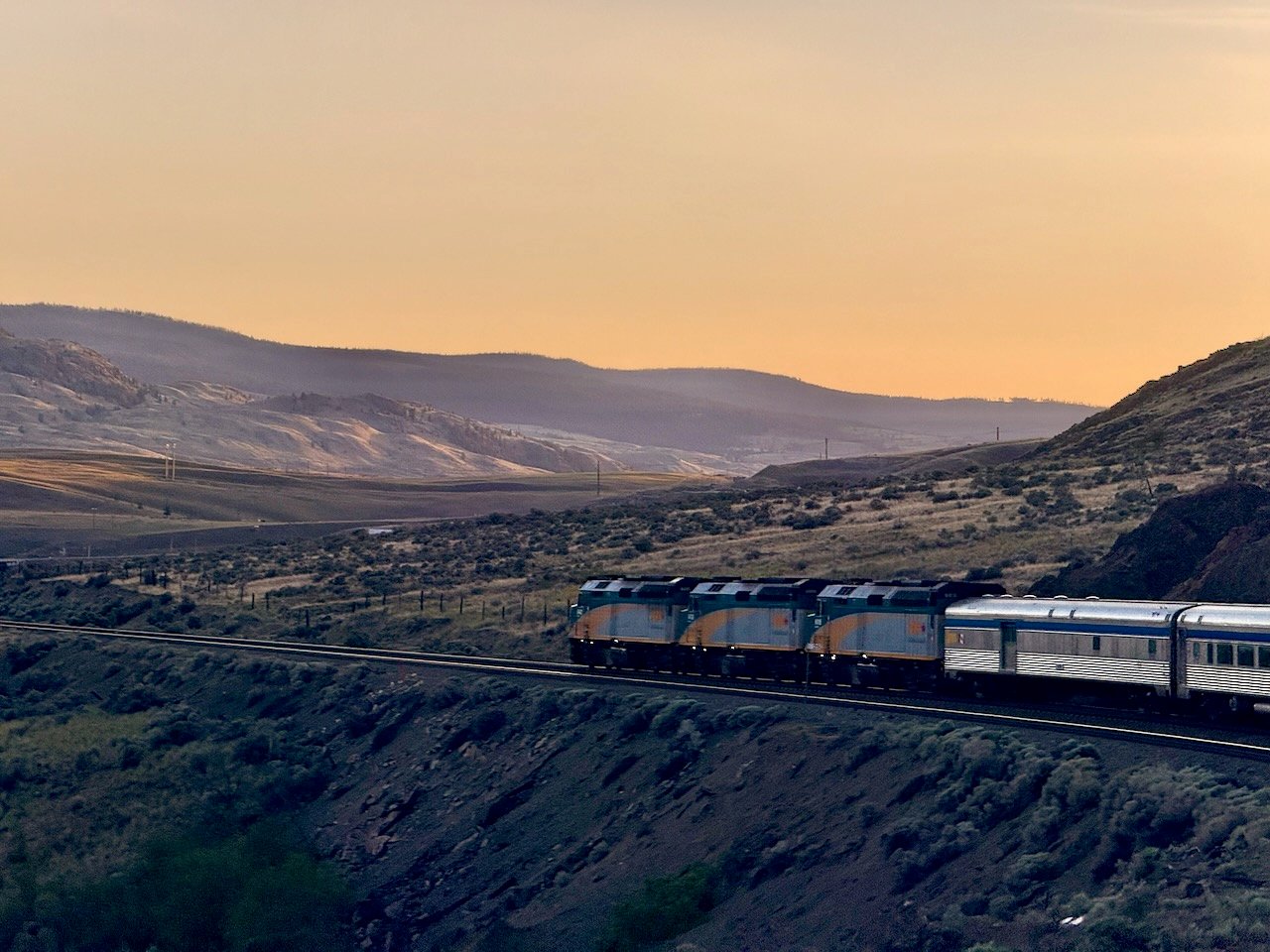 Train traveling through scenic mountain landscape at sunset.