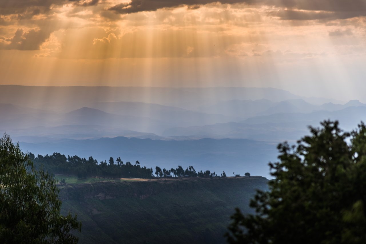 Sun rays streaming through clouds over scenic mountain landscape.