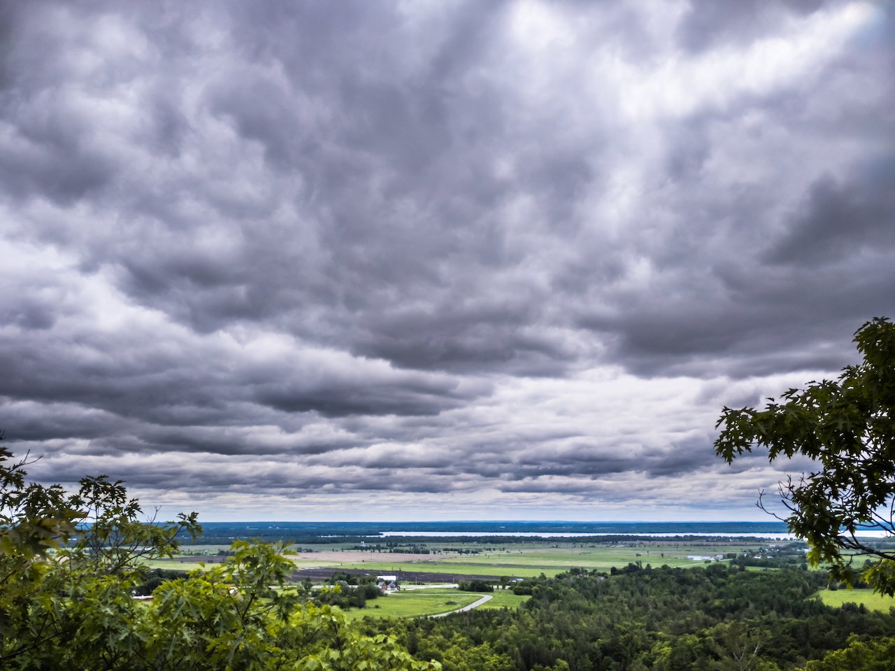 Stormy sky over lush green landscape with trees and fields.