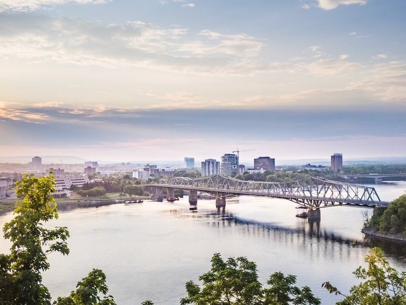 A city river at sunset, featuring a bridge and skyline in golden light.