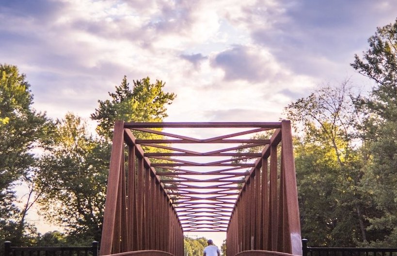 A cyclist crossing a geometric red bridge under a dramatic sky.