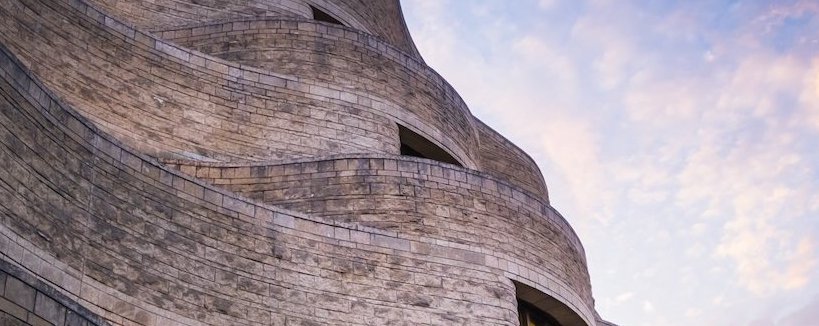 A curved stone building against a dynamic sky with golden-hour clouds.