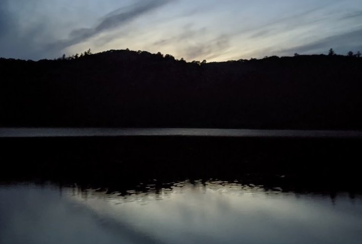 A lake at dusk with dark silhouettes of hills and a fading sky.