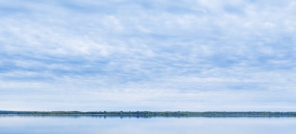 A calm lake reflecting a cloudy sky in a minimalist, almost monochrome composition.