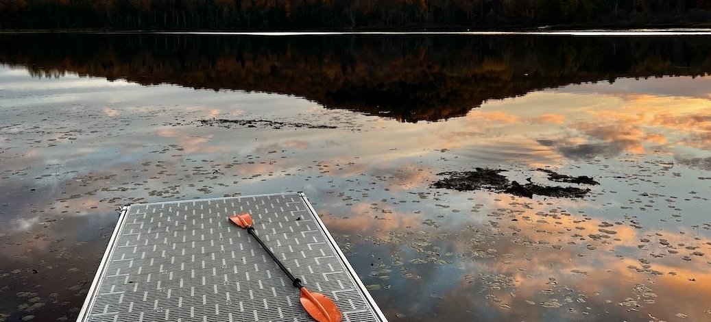A dock extending into a calm lake, reflecting autumn foliage under a colorful sky.