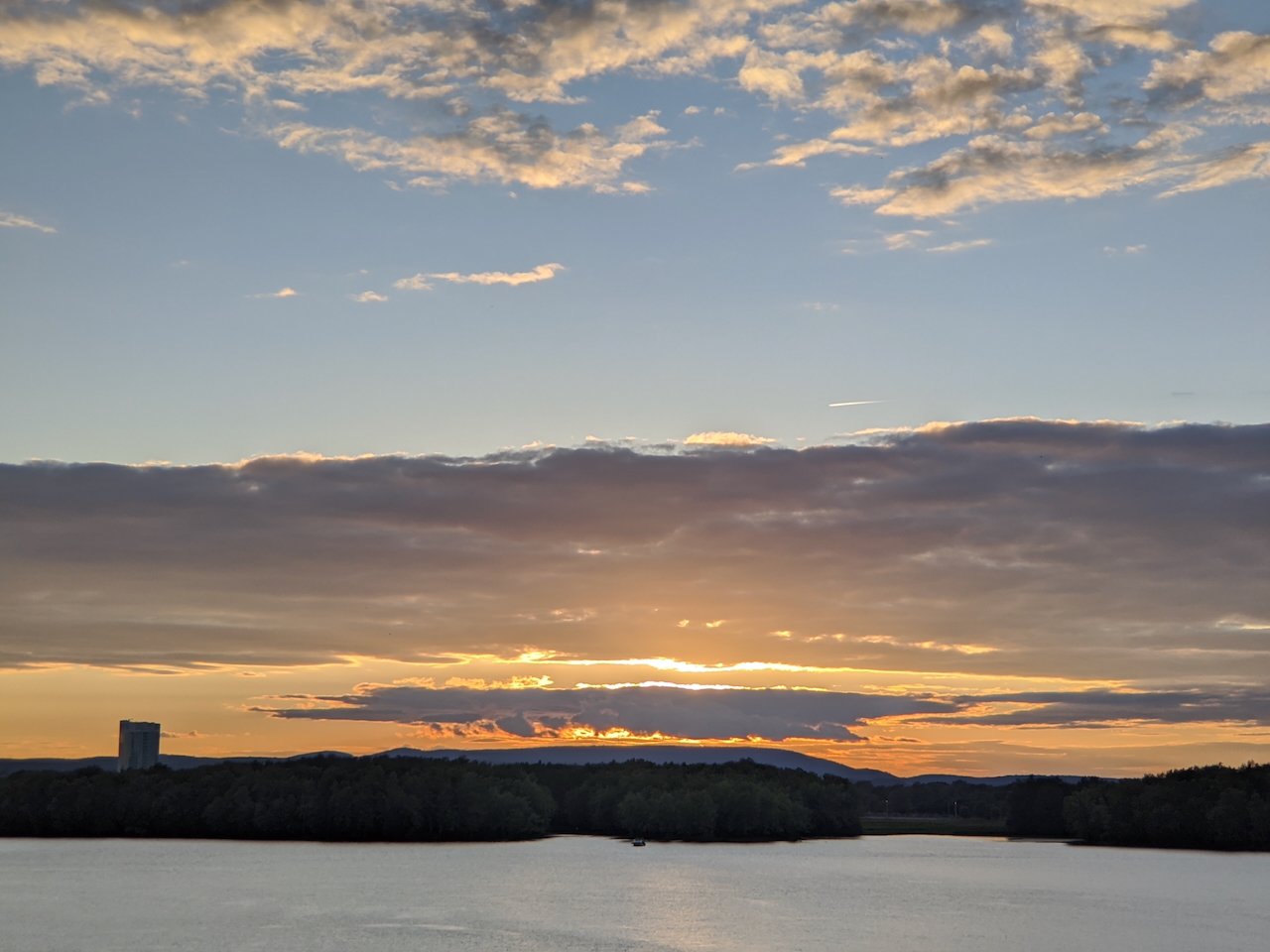 Sunset over a serene lake with clouds and distant hills.