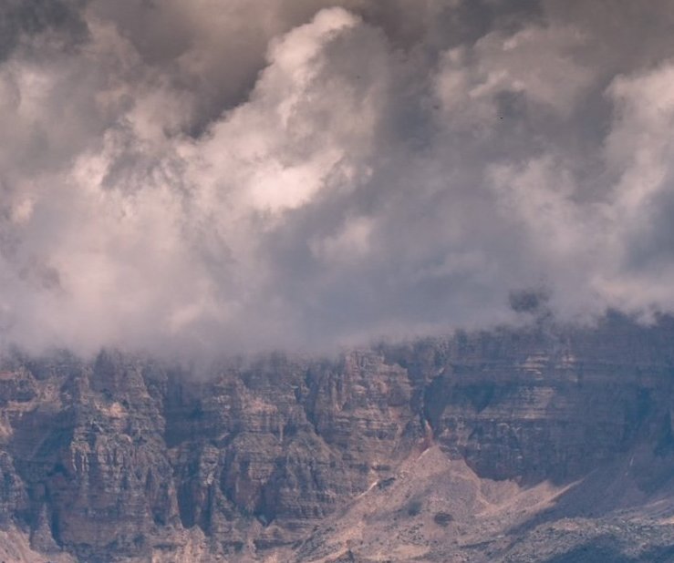 A rugged mountain landscape partially covered by thick dramatic clouds.