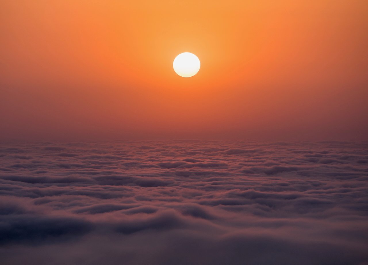 Sunset above a sea of clouds with a warm orange sky.