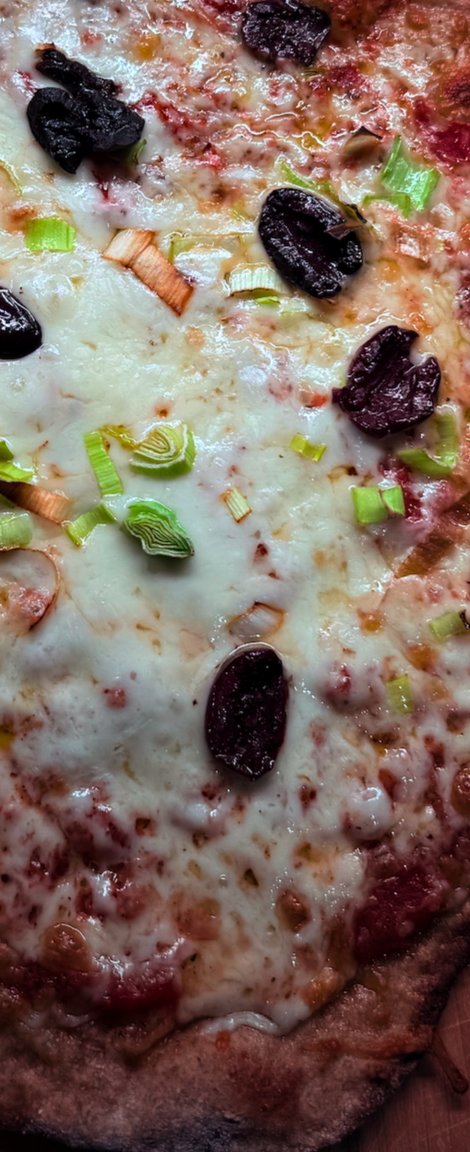 Baked cheese pizza with olives and scallions on a wooden board