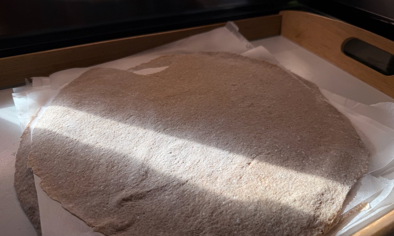 Flatbread dough rolled out on parchment paper in a wooden tray