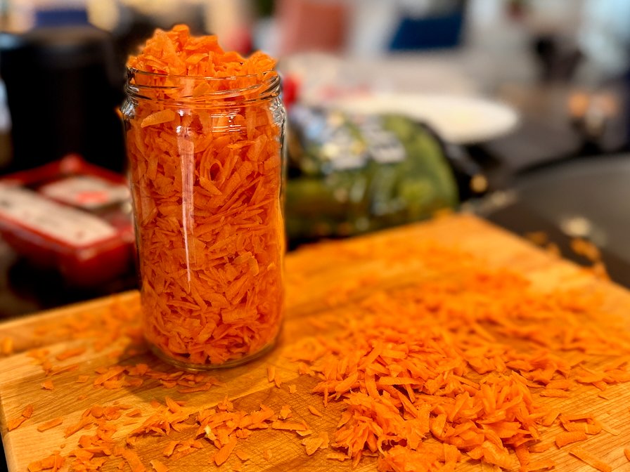 Jar of grated carrots on wooden cutting board in kitchen