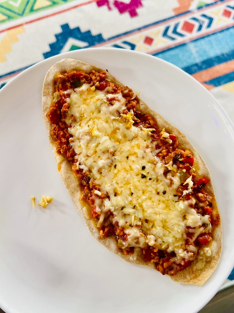 Mini flatbread pizza topped with tomato meat sauce and melted cheese on a white plate