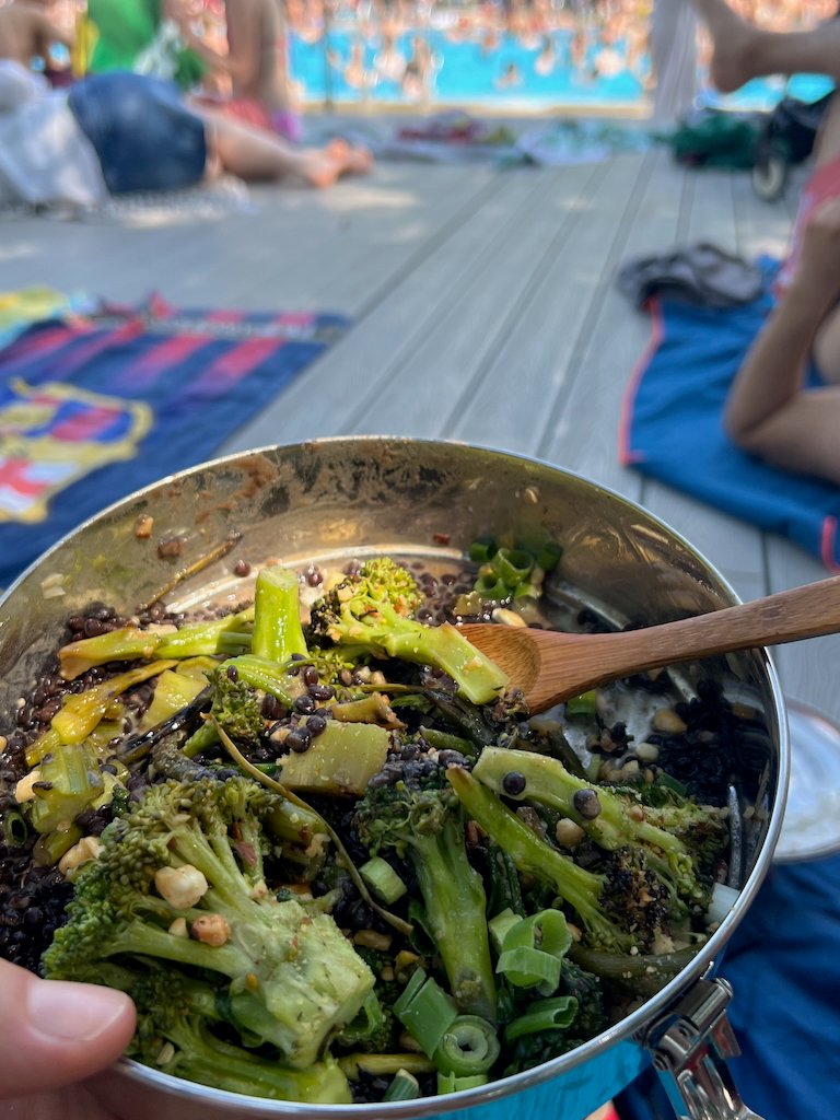 Lentil and broccoli salad in metal bowl at outdoor swimming pool setting