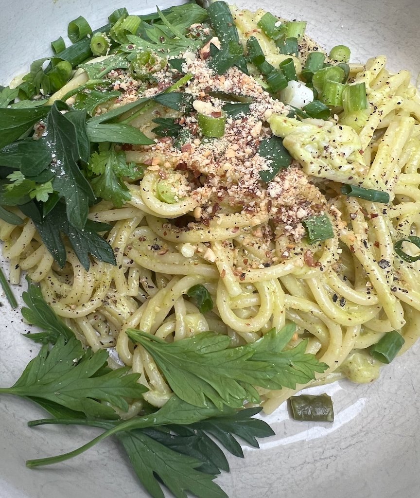 Creamy pasta with asparagus, green onions and herbs topped with crushed nuts