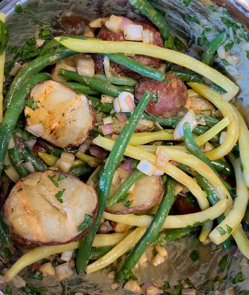 Colorful potato salad with green and yellow beans in a metal bowl