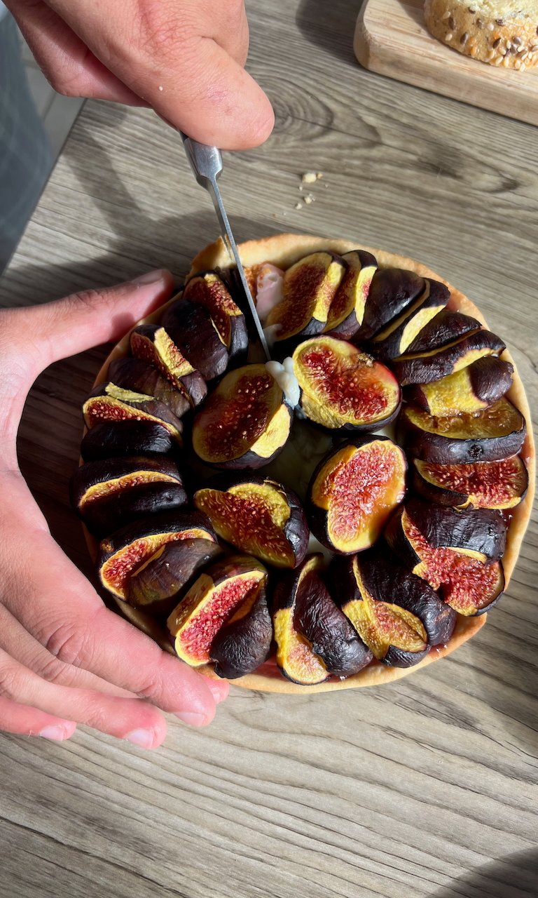 Fresh fig tart being sliced by hand on wooden table