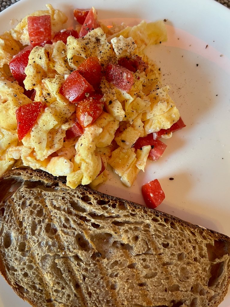 Scrambled eggs with tomato and toasted bread on a white plate