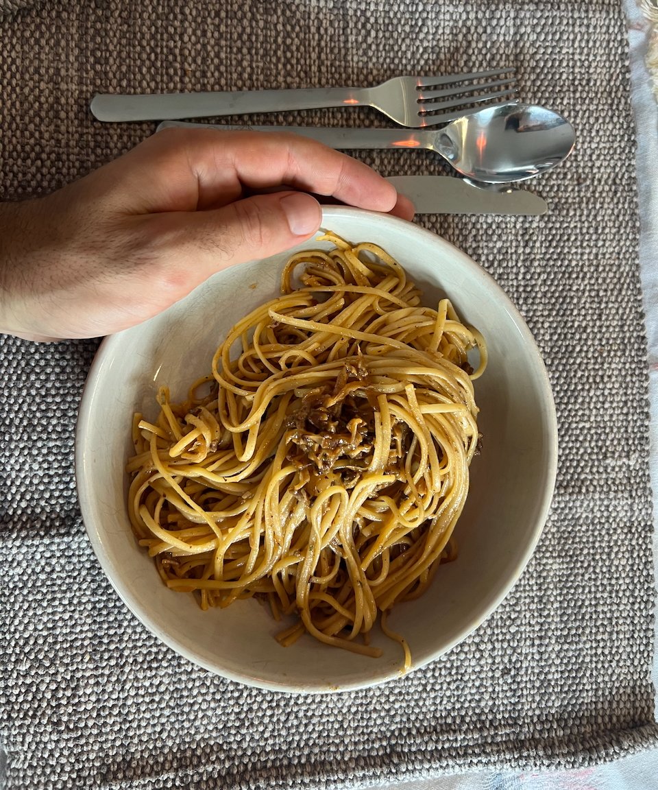 Hand beside bowl of spaghetti on placemat with cutlery
