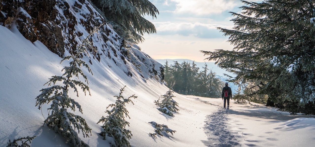 Snow-covered mountain path with hiker and soft sunlight in background