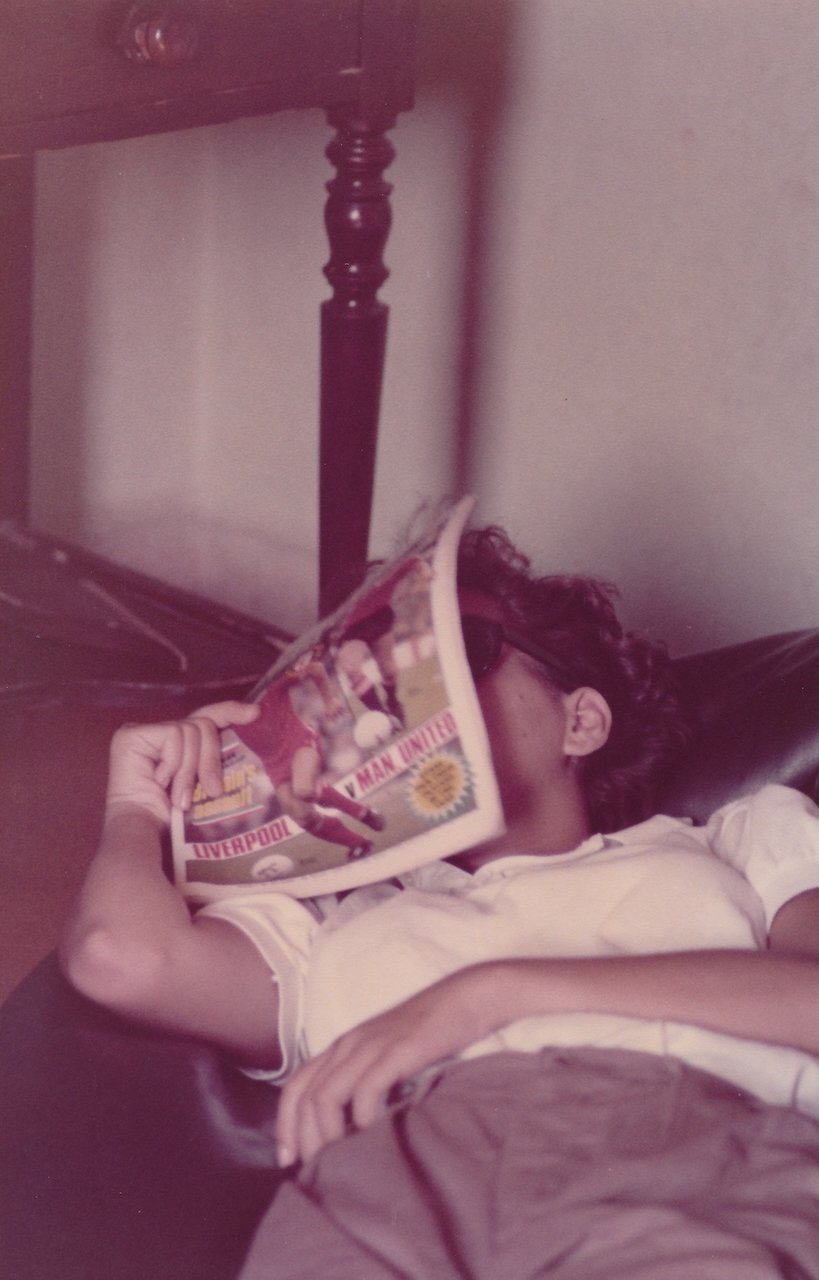 Person relaxing with a magazine covering their face, featuring a Liverpool vs. Man United cover.