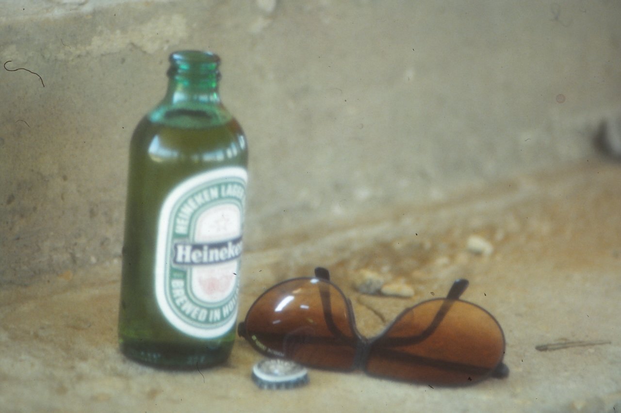Heineken bottle and sunglasses on a concrete surface.