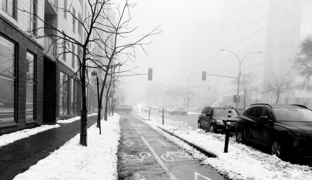 Foggy winter city street with bike lane and snowy sidewalks
