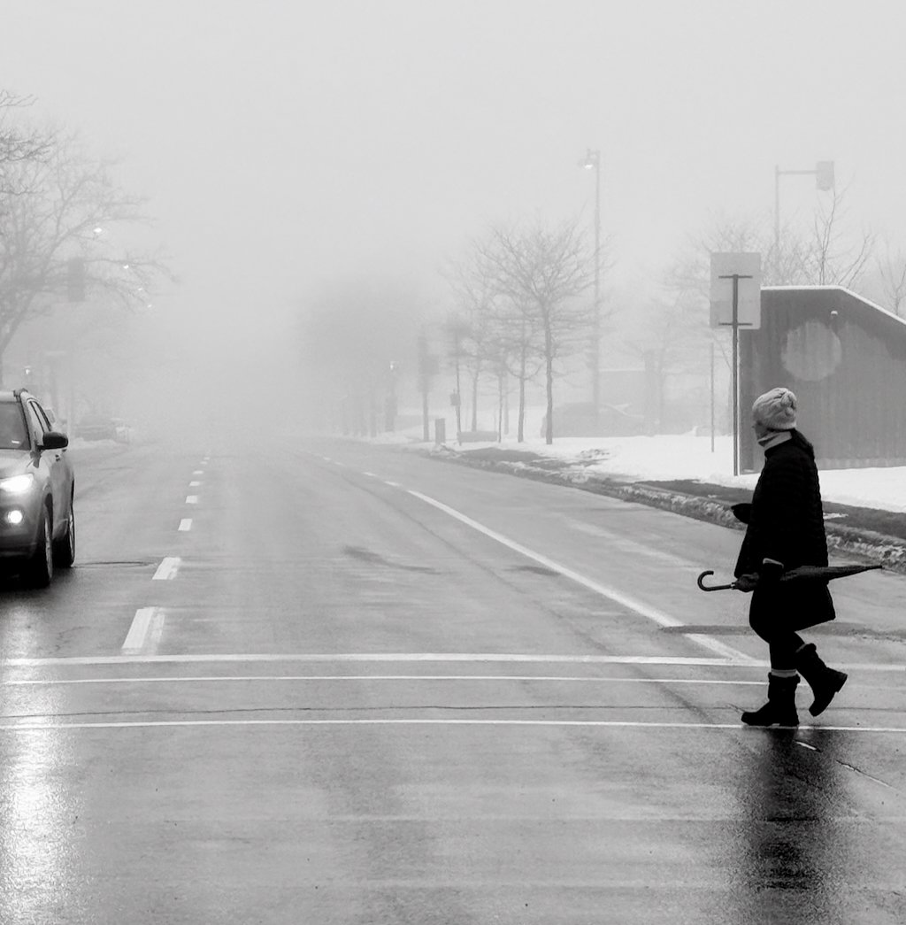 Pedestrian crossing foggy street with umbrella on a snowy day