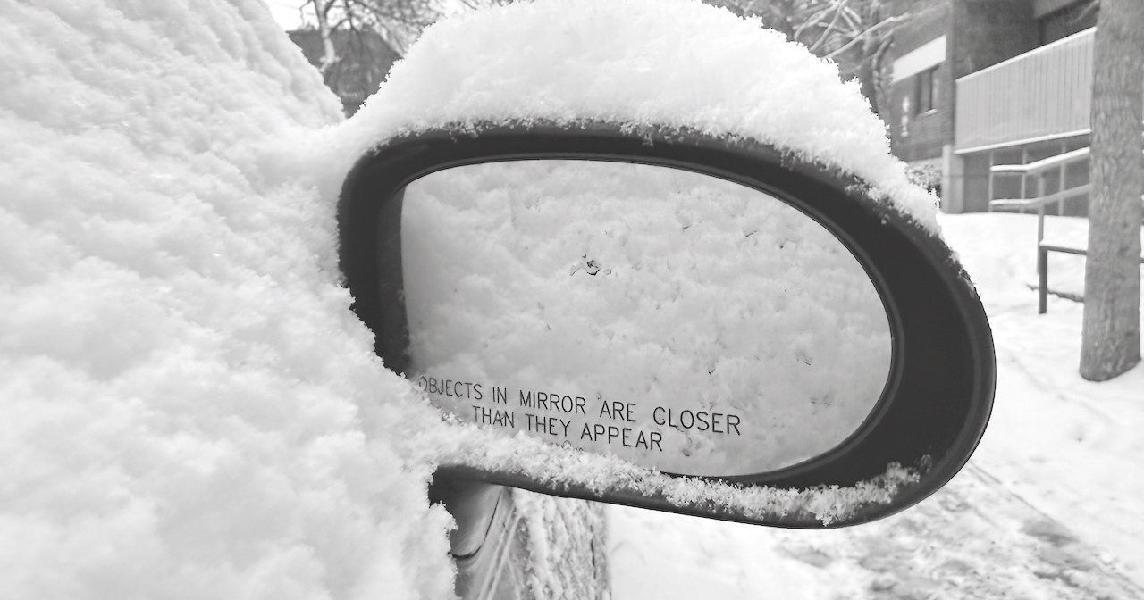 Snow-covered car side mirror with winter reflections