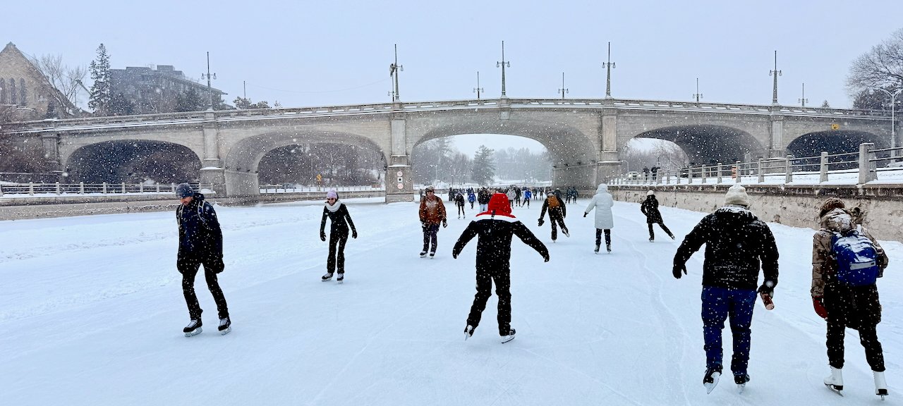 People ice skating under a bridge on a snowy canal in winter